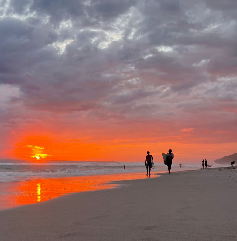 Sunset with surfers walking on the beach